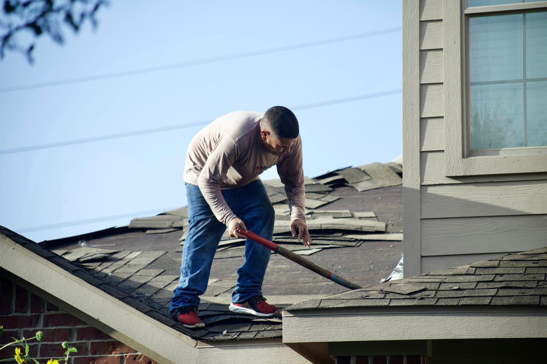 A contractor up on a customer's roof, hammer in hand, phone in his pocket.